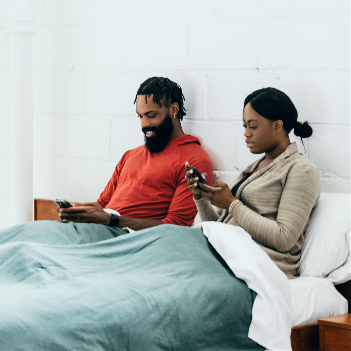 A couple sitting up in bed on their phones, showing a mattress with motion isolation for two sleepers.