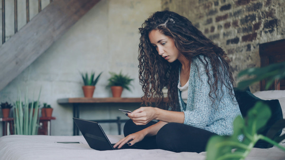 A person working on a laptop in bed on a supportive mattress in a cozy plant-filled bedroom.