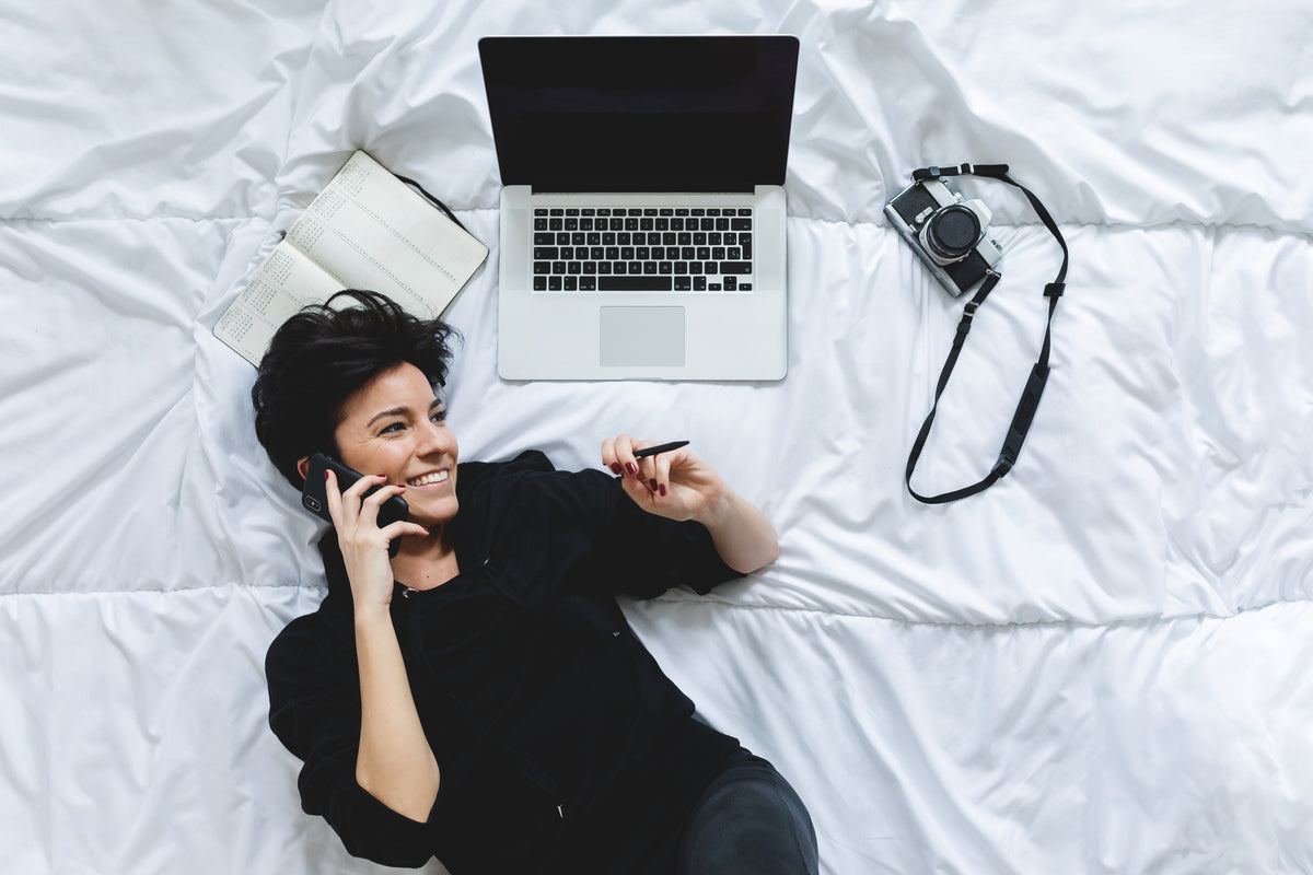 A person relaxing on a comfortable mattress with white bedding while using a phone.